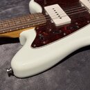 Detail elektrické kytary s bílým korpusem a hnědým hmatníkem. Kytara má červeně vzorovaný pickguard a dva bílé snímače s jednoduchými cívkami. Povrch…
