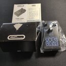 Černý kytarový pedál v originální plastové fólii s nápisy TUBE CAKE, TC-3, 2 WATT LITHIUM BATTERY a AMT Electronics. Na pedálu jsou vidět ovladače VO…