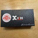 Černá papírová krabice s nápisem Xvive a označením L2 Wireless Guitar System. Na víku je nalepená kulatá bílo-červená nálepka s textem WARRANTY 4 YEA…