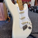 Bílá elektrická kytara typu Stratocaster s bílým pickguardem a javorovým hmatníkem. Nástroj má tři snímače s krémovými plastovými krytkami, tři poten…