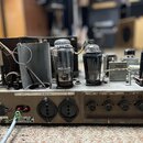 Zadní strana starého elektronického zařízení v kovovém šasi hnědé barvy. Na horní části jsou vidět vakuumové elektrony, kondenzátory a zapojení kabel…