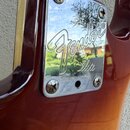 Detail zadní části kytary s hnědým lakem. Je zde vidět chromovaný kryt s vyraženými nápisy Fender® a Elite. Kryt je připevněn čtyřmi šrouby, z nichž…