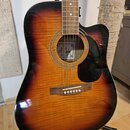 Akustická kytara s cutawayem v barevném provedení sunburst. Na štítku uvnitř ozvučovacího otvoru je nápis M. Parker a text "Handcrafted in USA". Kyta…