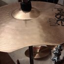 Mosazný činel s koncentrickými rýhovanými kruhy, umístěný na chromovaném stojanu. Na povrchu je černý nápis PAISTE, pod ním model 2011 a slovo BRONZE…