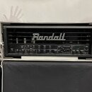 Černý kytarový zesilovač značky Randall umístěný v transportním kufru. Na předním panelu jsou ovládací knofíky a přepínače s nápisy GAIN, LEVEL, BASS…