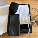 V otevřené černé krabici se nachází černý mikrofonní popfiltr z pěny a černý kožený pouzdro se zipem. Vedle nich je položen bílý papírový návod s náp…