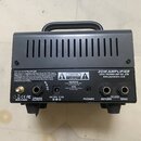Zadní strana šedého zesilovače s černou rukojetí. Na zařízení je bílý nápis 20W AMPLIFIER, JOYO TECHNOLOGY CO.,LTD a web www.jeyoaudio.com. Jsou zde…