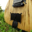 Detailní pohled na tělo elektrické kytary z masivního dřeva s výraznou žlutohnědou strukturou slz. Nástroj má černé snímače a černý kobylník. V dolní…