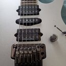 Detail bílé elektrické kytary s třemi černými humbuckery. Na každém snímači je bílý nápis DiMarzio/ibz. Kytara má chromovaný tremolo systém s viditel…