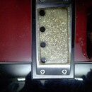 Detailní pohled na elektrický snímač s kovovým rámečkem, který je osazen do červeného trupu nástroje. Snímač má zlatavý, zrnitý povrch a čtyři vidite…