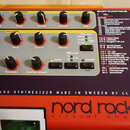 Detailní pohled na ovládací panel červeného syntetizátoru s nápisem nord rack 2 virtual analog a VIRTUAL ANALOG SYNTHESIZER MADE IN SWEDEN BY CLAVIA.…