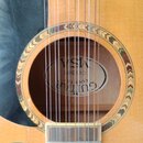Detail akustické kytary s přirozenou dřevěnou barvou a černým plektrem. Uvnitř ozvučnice je vidět štítek s nápisy GUITAR COUNTR CW1500 MSA. Kolem otv…