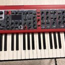 Červený digitální syntezátor s klávesnicí. Na horním panelu jsou viditelné nápisy SYNTH, EXTERN, EFFECT 1, EFFECT 2, DELAY, AMP SIM/EQ a COMPRESSOR.…