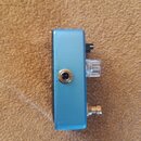 Modrý kytarový efekt s kovovým šasi. Na boku jsou vidět jeden vstupní jack konektor, jeden ovládací knoflík z průhledného plastu a jeden přepínač. Po…