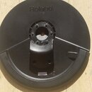 Černý plastový pad s logem Roland a nečitelným označením modelu pod ním. Uprostřed se nachází kruhová plocha s několika šrouby a uprostřed otvorem. V…
