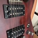 Detail korpusu elektrické kytary v tmavě červené barvě. Nástroj má dva černé humbuckery, přičemž na spodním je bílý nápis Seymour Duncan. Jsou vidět…