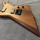 Elektrická kytara s hrotovitým tělem z dřeva s viditelnou masivní strukturou. Nástroj má dva humbuckery, dva ovládací knofíky a černý kobylník s nápi…