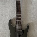 Černá elektrická kytara s černým hardwarem a tmavým hmatníkem. Na hlavě je svisle napsaný bílý nápis Ibanez. Kytara má dva humbuckery, jeden ovládací…