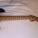 Černá elektrická kytara s hnedým javorovým hmatníkem a hlavou. Na hlavě je černý nápis Squier STRATOCASTER a pod ním menší text MADE IN CHINA. Nástro…