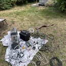 Sada zvukové techniky rozložená na bílé plátno s květinovým vzorem na trávníku. Soubor obsahuje dva šedé reproduktory, černý mixovací pult, mikrofonn…