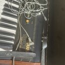 Černý klávesový nástroj značky YAMAHA s nápisy SK10 a SYMPHONIC ENSEMBLE. Na povrchu jsou vidět ovládací prvky, včetně žlutého knoflíku s nápisem VOL…