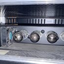 Černý rackový zesilovač umístěný v transportním kufru. Na levém panelu je nápis MESA Engineering a označení modelu TriAxis, dále jsou zde vstupy INPU…