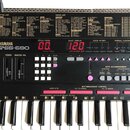 Černý digitální klávesový nástroj s bílými a černými klávesami. Na předním panelu je bílý nápis YAMAHA a model PSS-590. Nástroj má dvě červené digitá…