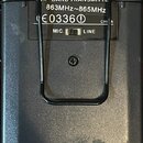 Černý plastový vysílač s kovovým klipem. Na štítku je nápis HF BAND TRANSMITTER, 863MHz~865MHz, symbol CE a kód 03360 s číslem 1 v kroužku, dále nápi…