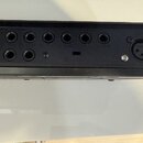 Záběr na zadní panel černého elektronického zařízení. Jsou vidět dvě řady jackových vstupů a dva XLR konektory. Povrch je matně černý s viditelným šr…
