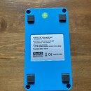 Zadní strana modrého efektpedálu z kovového materiálu. Uprostřed je bílá náleplka s textem: „INPUT: 1/4" mono audio jack (impedance: 470k Ohms) OUTPU…