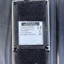 Záběr na zadní stranu kytarového pedálu s kovovým šasi a černým suchým zipem. Uprostřed je bílý štítek s nápisy USE 9V DC CENTRE NEGATIVE POWER SUPPL…