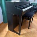Černý digitální piano v konzolovém provedení s přiloženou černou stolečkou. Na horní části nástroje je vidět nápis Roland a na notovém pulpitu je umí…