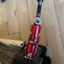 Detailní záběr na červený kovový mechanismus s kloubem, který je součástí hudebního příslušenství. Horní část tvoří černá lišta s řadou otvorů a stří…