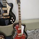 Polodupatá elektrická kytara s červeným gradientem a černým okrajem. Na hmatníku je nápis „Jolana“. Kytara má bílý pickguard, dva snímače a dvě bílé…