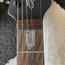 Detail hmatníku a hlavy černé basové kytary. Na hlavě je bílý nápis Sterlite by MUSIC MA. Hmatník je vyroben z tmavého dřeva s vložkou ve tvaru štítu…