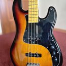 Elektrická basová kytara s korpusem v barevném přechodu od žluté přes oranžovou k červené a černé. Nástroj má černý pickguard, čtyři ovládací knofíky…