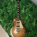 Elektrická kytara typu Les Paul v žlutohnědé barvě s hnědým přechodem. Na hlavě je nápis "Epiphone" a logo. Kytara má dva humbuckery, čtyři ovládací…
