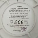 Fotografie zachycuje spodní část bílého plastového zařízení s圆形 štítkem. Na štítku je uveden text: „Dohm Sound Conditioner Schlafhilfe SleepMate“, „A…