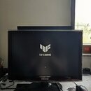 Na fotografii je černý počítačový monitor značky SAMSUNG. Uprostřed vypnuté obrazovky je bílé logo a nápis TUF GAMING. Monitor stojí na černém kulaté…