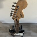 Fotografie zachycuje hlavu a hmatník elektrické kytary v přirozené dřevěné barvě. Na zadní straně hlavy je nápis Squier STRAT® a logo Fender, v horní…