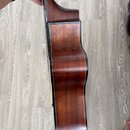 Boční pohled na korpus akustické kytary z hnědého dřeva s viditnou masivním kresbou. Instrument má tmavý lem po obvodu korpusu a hladký lakovaný povr…