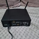 Černý bezdrátový přijímač s dvěma anténami. Na zadní straně jsou dva konektory s nápisy AUDIO OUT 1 BALANCED a AUDIO OUT 2 BALANCED a vstup DC ONLY 1…