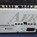 Zadní strana bílého akustického komba v černém pouzdře. Na panelu je velký šedý nápis AER a pod ním text Compact 60 twin channel acoustic amplifier.…
