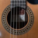 Detail rozetky akustické kytary s dřevěnou deskou světlé barvy. Uvnitř otvoru je vidět štítek s nápisy Jose Ramirez, MADE IN SPAIN a STUDIO GUITAR. N…