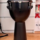 Černý djembe s matným povrchem a bílou membránou. Horní obruč je kovová a stahovací systém tvoří kovové háky s černými plastovými krytkami. V dolní č…