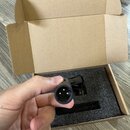 Fotografie zachycuje ruku držící černý kabel s konektorem typu XLR. Kabel je umístěn nad otevřenou hnědou kartonovou krabicí s černou pěnovou výplní.…
