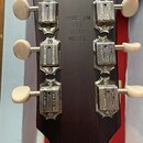 Záběr na zadní stranu tmavě hnědé hlavy kytary. Na dřevěném povrchu je vyrazeno sériové číslo 140018206 a nápis MADE IN USA 2014 MODEL. Jsou vidět še…