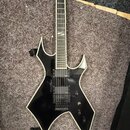 Černá elektrická kytara s ostrými hranami korpusu a bílým lemováním. Na hmatníku jsou vidět vložky s nápisem "Jackson". Nástroj má dva humbuckery, je…