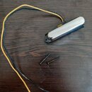 Na tmavé dřevěné desce leží černý magnetický snímač s chromovaným krytem a dvěma přilehlými šrouby. Ze snímače vycházejí dva dlouhé vodiče, jeden v č…