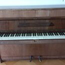Hnědé dřevěné piano s klaviaturou. Na horní části nad klávesami je vyryt nápis BECHSTEIN. Povrch dřeva vykazuje známky opotřebení a škrábance, zejmén…